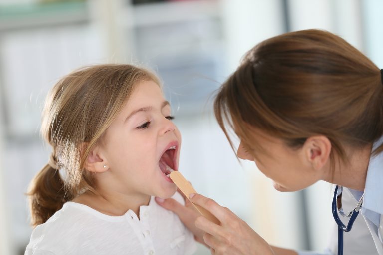 Ärztin untersucht Hals und Mund eines jungen Mädchens.